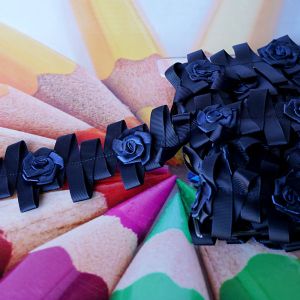 Detailansicht eines dunkelblauen Dekobandes in Zickzack-Form, verziert mit 3cm grossen Satinrosen auf aufgereihten Farbstiften bei Spitzentraum.ch.