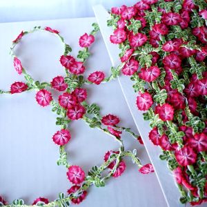 Nicht elastische Blumenborte (15mm) aus weichem Webband gefaltet mit plastischen Blumen in Fuchsia und Gr&uuml;n, aufgewickelt auf einer Karte bei Spitzentraum.ch.