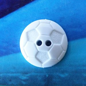 Runder, weisser Kunststoffknopf (18mm) im Fussball-Design mit gepr&auml;gtem Wabenmuster und zwei L&ouml;chern mittig auf blauem Grund bei Spitzentraum.ch.