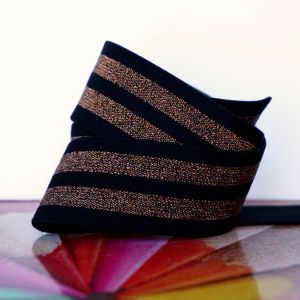 Aufgewickeltes elastisches Gummiband in Schwarz mit zwei gl&auml;nzenden ros&eacute;goldenen Streifen.