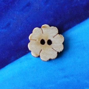 Ein einzelner, naturbelassener 10mm Kleeblatt-Holzknopf mit 2 L&ouml;chern und rustikal angekokelten Kanten vor blauem Hintergrund bei Spitzentraum.ch.