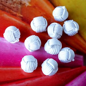 Zehn kugelf&ouml;rmige Kn&auml;uelkn&ouml;pfe in der Farbe Weiss. Die Oberfl&auml;che aus feiner Satinkordel imitiert die Wicklung eines Wollkn&auml;uels und verleiht eine tolle Haptik.