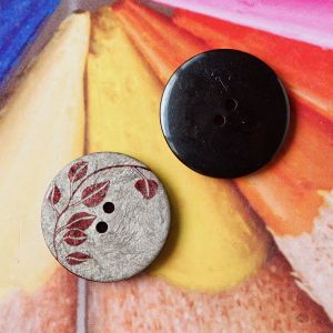 Zwei 17mm Kn&ouml;pfe mit dunkelrotem Blattmuster zur Ansicht der marmorierten Taupe-Vorderseite und der glatten, schwarzen R&uuml;ckseite f&uuml;r Spitzentraum.ch.