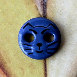 Runder, 12mm grosser Motivknopf in dunkelblau mit aufgedrucktem schwarzem Katzengesicht und zwei L&ouml;chern als Augen.