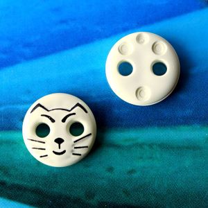 Zwei ecrufarbene Katzenkn&ouml;pfe (12mm) aus Kunststoff zur Ansicht der Vorderseite mit dem schwarzen Tiermotiv und der leicht strukturierten, glatten R&uuml;ckseite.