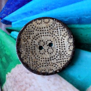 Nahaufnahme eines 39mm Kokosnuss-Knopfs mit fein gepr&auml;gtem polynesischem Punktmuster auf naturbelassener Oberfl&auml;che vor gr&uuml;nem Grund auf Spitzentraum.ch.