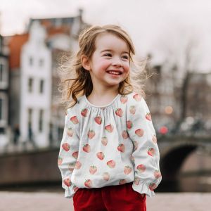 Musselin Stoff mit roten Erdbeeren auf weiss - das Bild zeigt ein Nähbeispiel: kleines Mädchen trägt eine Bluse aus diesem Musselin.
